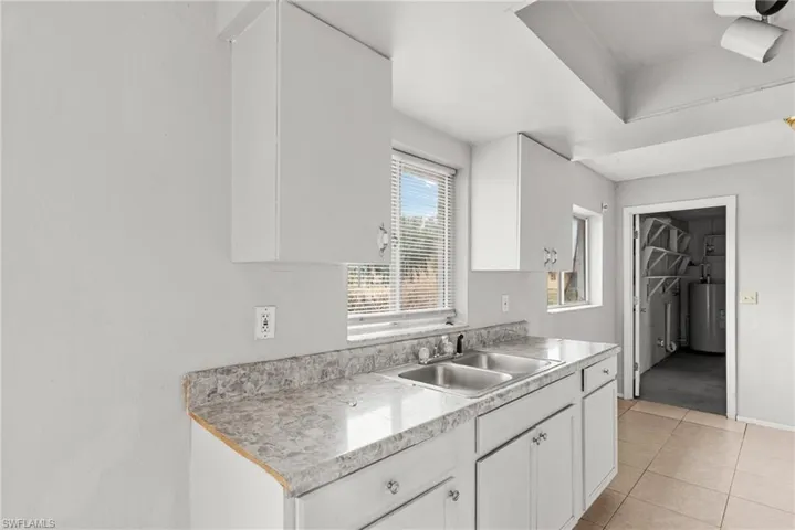 Kitchen featuring white cabinets, light countertops, light tile patterned floors, and water heater