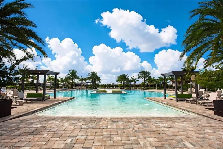 Swimming pool featuring a sun shelf, paved stone deck, and integrated wooden pergolas surrounded by palm trees