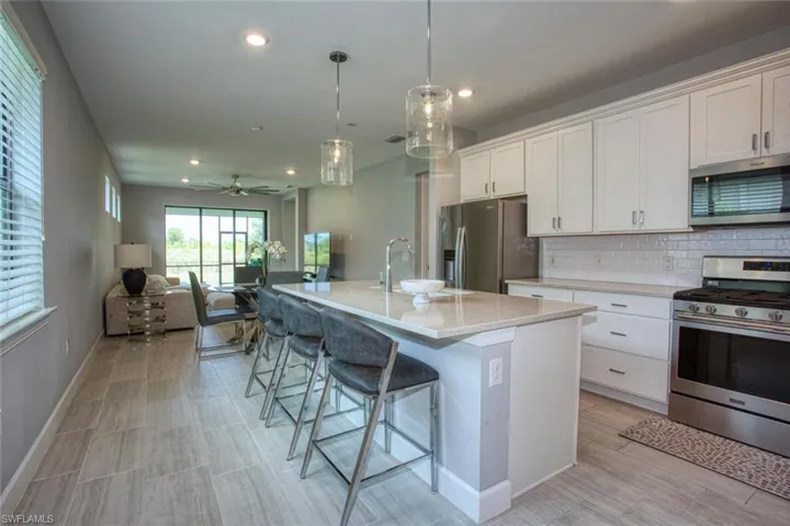 Kitchen featuring white cabinetry, quartz countertops, a central island with a stainless steel sink, tile backsplash, and stainless steel appliances