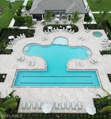 Community swimming complex featuring a custom-shaped pool, dedicated lap lanes, an elevated spa, expansive stone paver decking, and a covered clubhouse structure