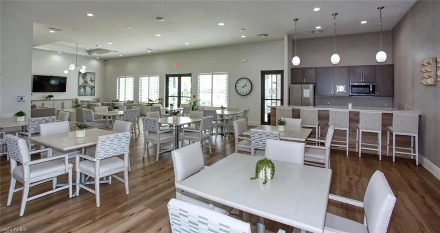 Open-concept common area featuring wood-finish flooring, recessed lighting, a kitchenette with dark cabinetry, and suspended pendant lighting above a built-in counter