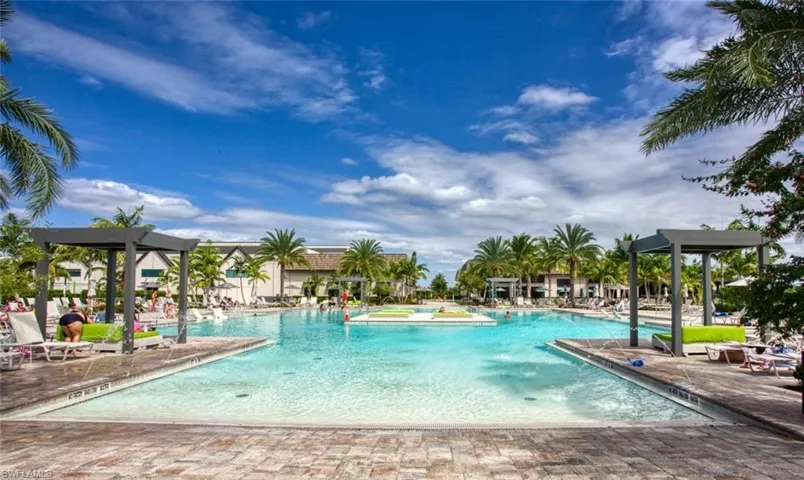 Resort-style swimming pool featuring a zero-entry design, built-in structural pergolas, stone paver decking, and mature palm landscaping