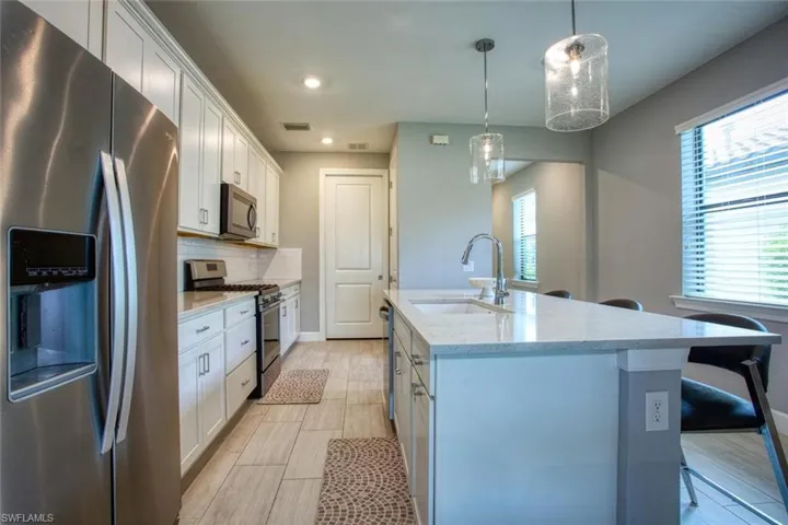 Kitchen featuring white shaker-style cabinetry, quartz countertops, a central island with an undermount sink, stainless steel appliances, and tile flooring