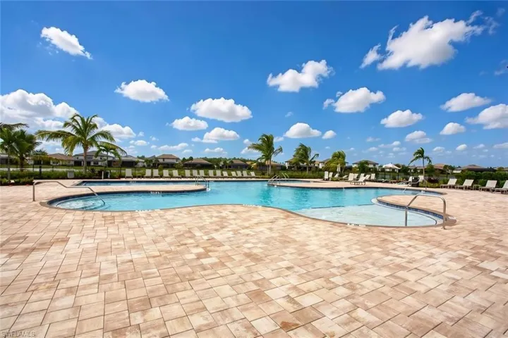 Resort-style pool with a sun shelf, paved deck, and mature palm trees