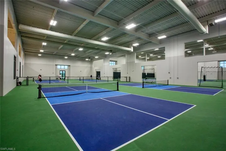 Indoor recreational facility featuring multiple pickleball courts, high ceilings with exposed ductwork, and overhead industrial lighting