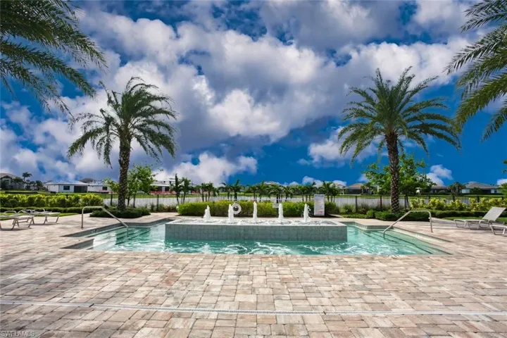 Pool area featuring a central water fountain, paver patio, perimeter palm trees, and metal handrails