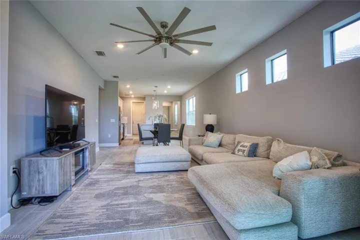 Open-concept area featuring light-toned wood-finish flooring, high ceilings with an oversized multi-blade ceiling fan, recessed lighting, and three high-set transom windows