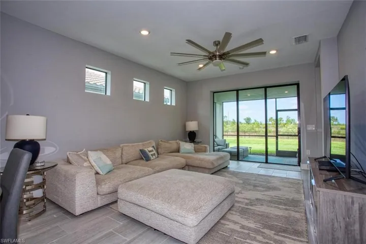 Living area featuring large-format tile flooring, recessed lighting, a multi-blade ceiling fan, three transom windows, and a multi-panel sliding glass door providing outdoor access