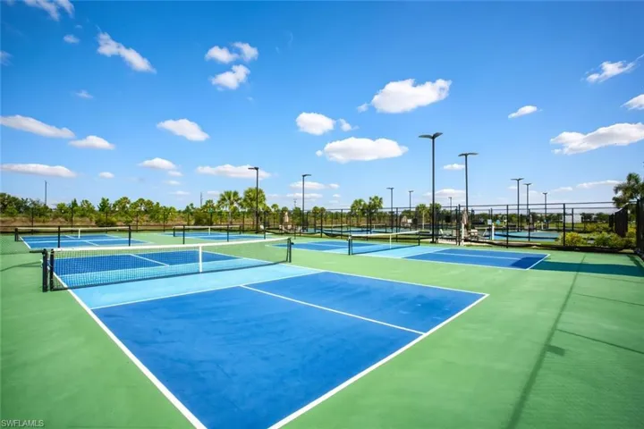 Multi-court recreational area featuring blue and green hard-surface surfacing, professional-grade netting, perimeter chain-link fencing, and overhead court lighting