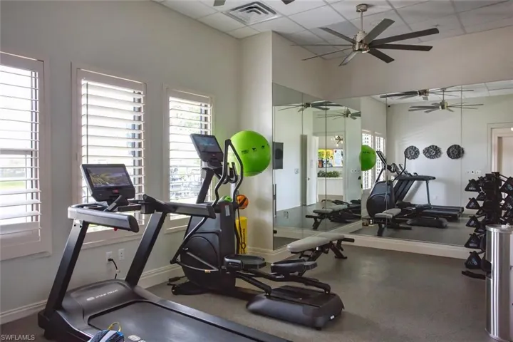 Fitness room featuring large wall mirrors, multi-blade ceiling fan, and plantation shutters