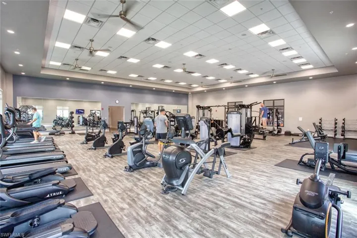 Fitness facility featuring drop-tile ceilings with recessed lighting, integrated ceiling fans, wall-to-wall mirrors, and wood-finish flooring