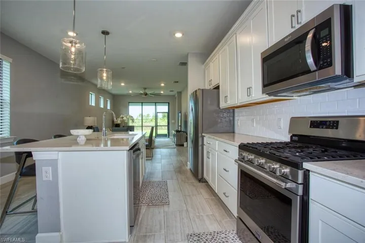 Kitchen featuring white shaker-style cabinetry, quartz countertops, a central island with a breakfast bar, stainless steel appliances, and subway tile backsplash