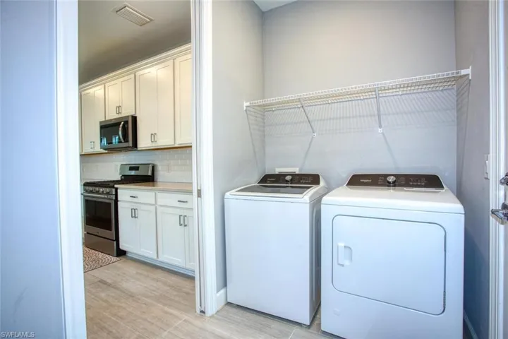 Laundry area featuring wire shelving and tile flooring, including a kitchen with white cabinetry, stainless steel appliances, and a tiled backsplash