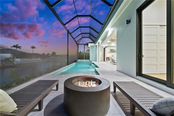 Pool at dusk featuring a water view, a lanai, a patio, an outdoor pool, and an outdoor fire pit
