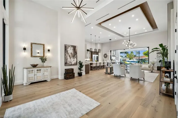 Living room featuring light wood finished floors, baseboards, an inviting chandelier, recessed lighting, and a high ceiling