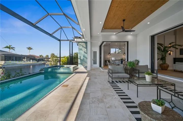 View of swimming pool featuring glass enclosure, a water view, a ceiling fan, a patio, and a pool with connected hot tub