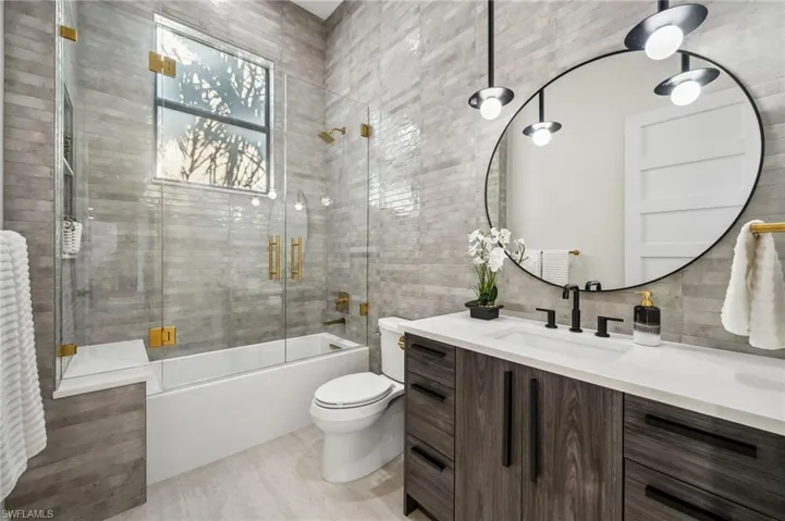 Full bath with toilet, vanity, and bath / shower combo with glass door