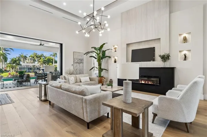 Living room featuring light wood-type flooring, a glass covered fireplace, a towering ceiling, and recessed lighting