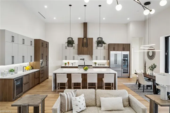 Kitchen with a towering ceiling, wine cooler, light countertops, light wood-style floors, and built in refrigerator