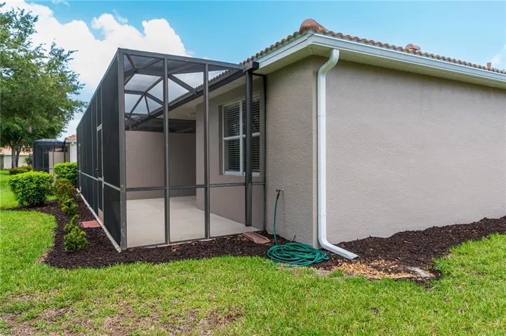 View of side of property featuring stucco siding, a tile roof, a patio, a lawn, and glass enclosure