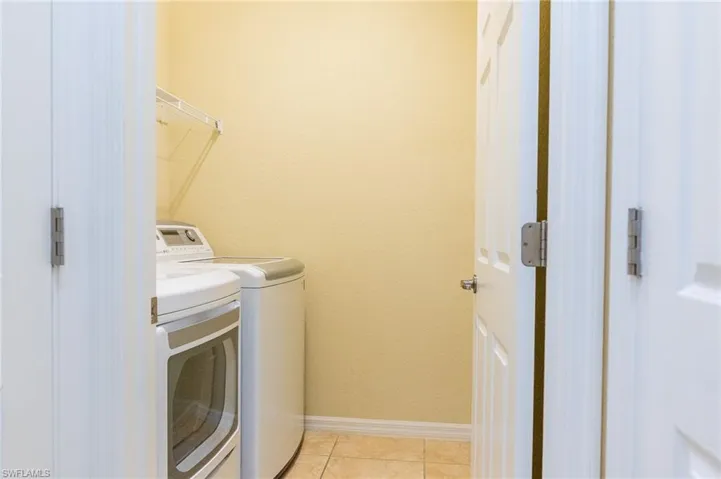 Laundry area featuring separate washer and dryer, light tile patterned floors, and baseboards