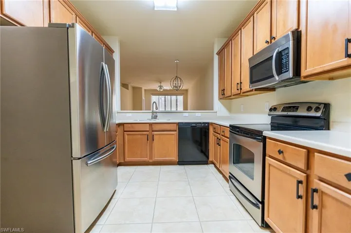 Kitchen featuring appliances with stainless steel finishes, a sink, light countertops, light tile patterned floors, and brown cabinets