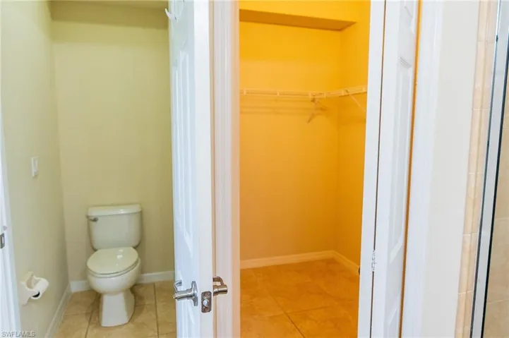 Bathroom with toilet, tile patterned floors, and a walk in closet