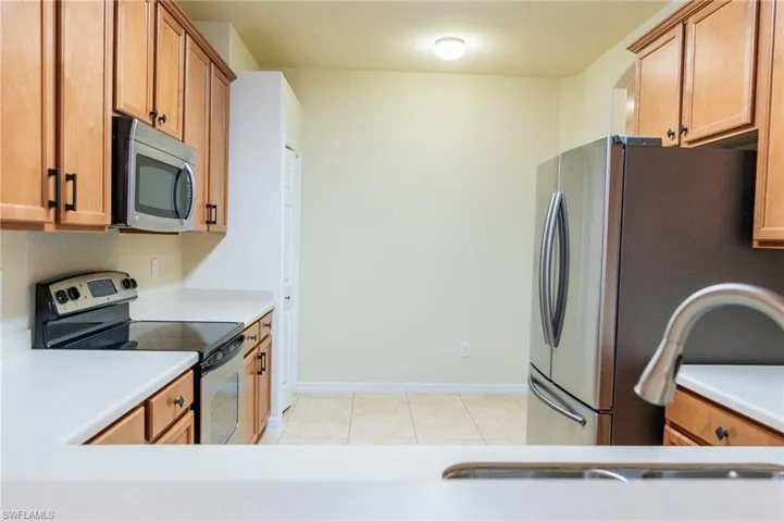 Kitchen featuring appliances with stainless steel finishes, light tile patterned flooring, light countertops, brown cabinets, and baseboards