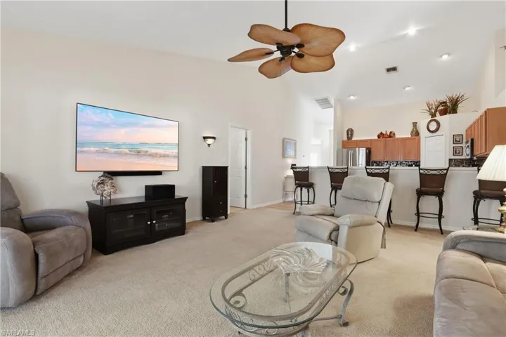 Living area featuring light carpet, ceiling fan, and lofted ceiling