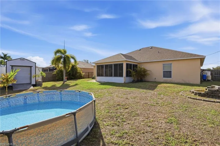 Rear view of house with a sunroom, a fenced backyard, stucco siding, and a storage shed