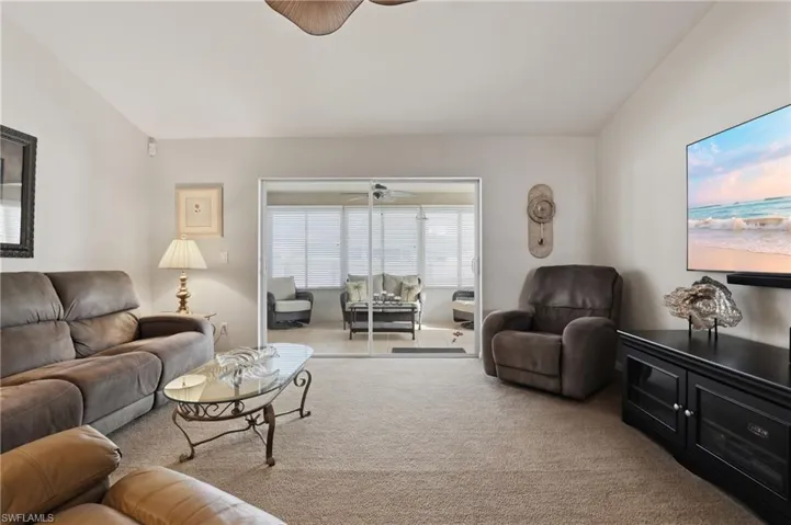 Carpeted living room featuring ceiling fan and vaulted ceiling
