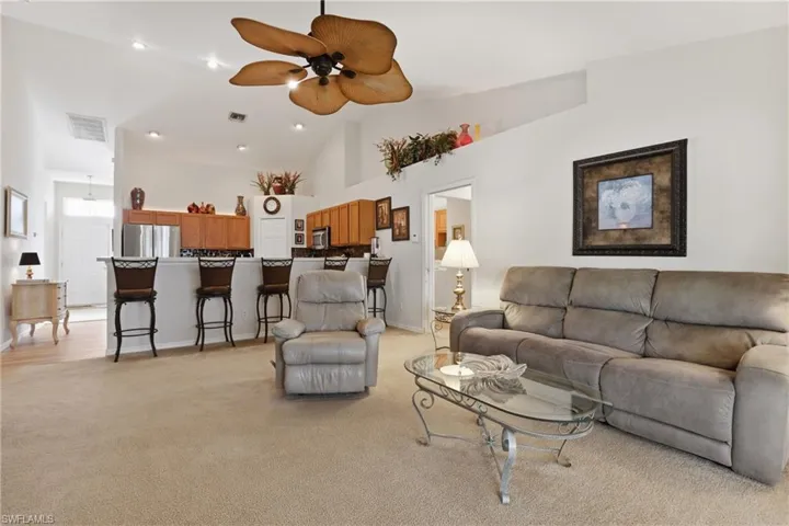 Living area with a ceiling fan, light colored carpet, and vaulted ceiling