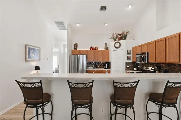 Kitchen with a breakfast bar, light countertops, stainless steel appliances, wood finish cabinets, and tasteful backsplash