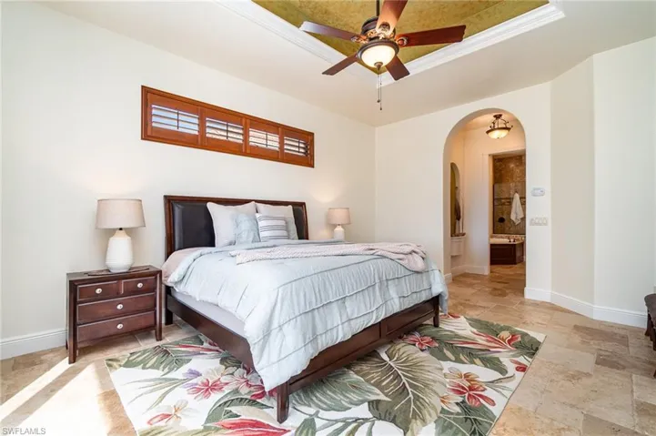 Bedroom with a raised ceiling, connected bathroom, and ceiling fan