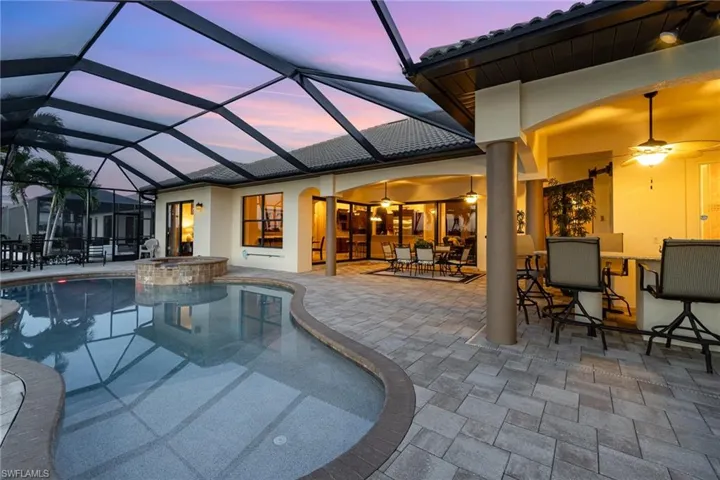 Pool at dusk featuring ceiling fan, a patio, and screen enclosure