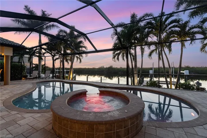 Pool at dusk with an in ground hot tub, a water view, screen enclosure, and a patio area
