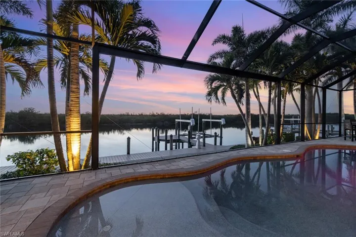 Pool at dusk featuring a water view, a boat dock, and screen enclosure
