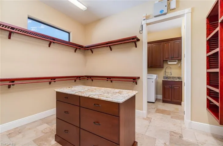 Walk in closet featuring an island, wood shelves and direct access to the laundry room.