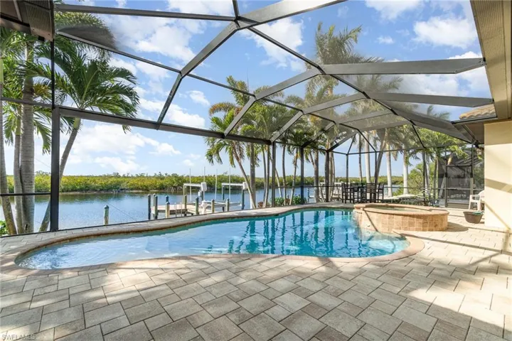View of swimming pool with a lanai, a patio, a water view, a boat dock, and an in ground hot tub
