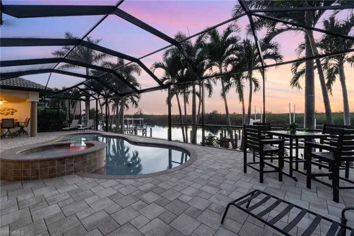 Pool at dusk with a water view, an in ground hot tub, a patio area, and screen enclosure