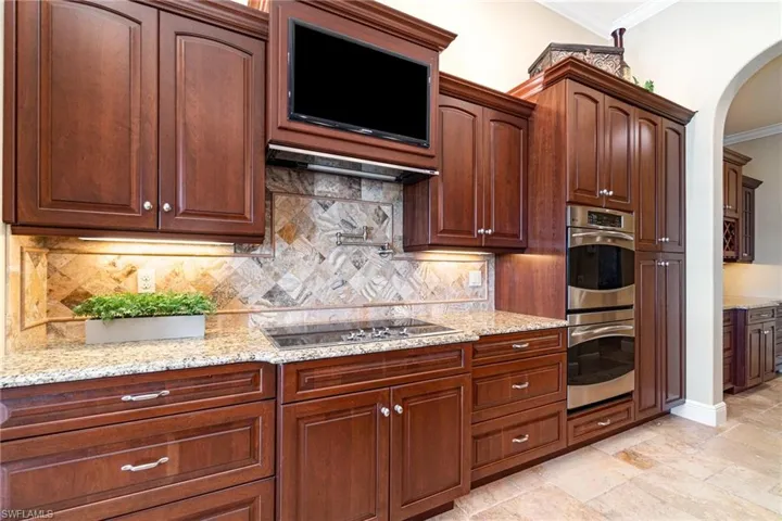 Kitchen featuring black stovetop, backsplash, crown molding, light stone countertops, and stainless steel double oven