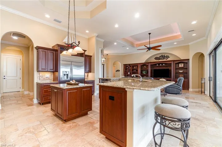 Kitchen featuring a breakfast bar area, a kitchen island with sink, hanging light fixtures, a tray ceiling, and stainless steel built in fridge