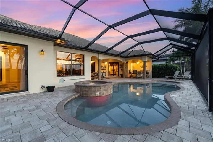 Pool at dusk with an in ground hot tub, a lanai, and a patio area