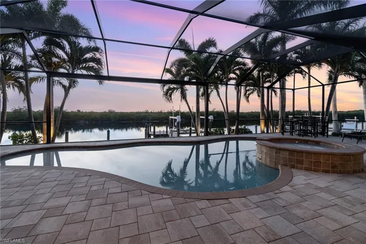 Pool at dusk featuring an in ground hot tub, a patio, screen enclosure, and a water view
