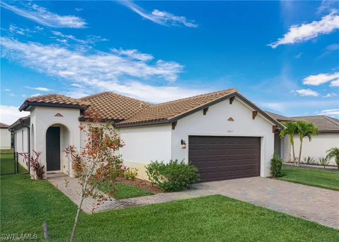 Exterior featuring a tiled roof, paver driveway, arched entryway, and landscaped front yard