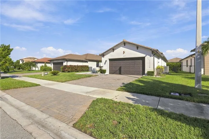 Stucco exterior with a tiled roof, paver driveway, and an attached two-car garage