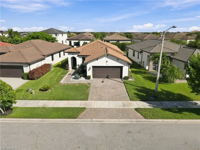 Mediterranean-style architecture with a tile roof, paver driveway, arched entryway, and mature landscaping