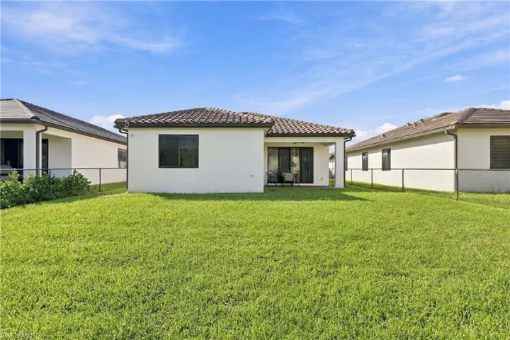 Expansive rear yard featuring green lawn, chain link fencing, a covered patio, and multi-pane sliding glass doors