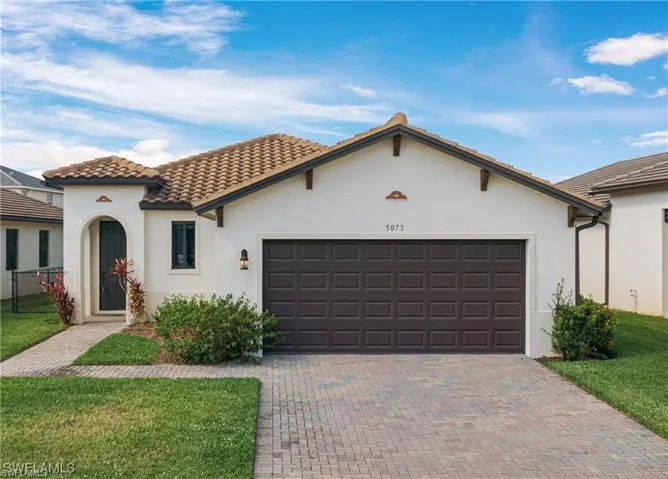 Stucco exterior with a tile roof, arched entry, paver driveway, and a two-car garage