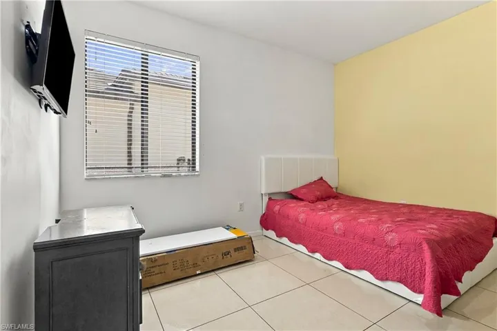 Window with horizontal blinds, neutral tone floor tile, and wall-mounted television bracket